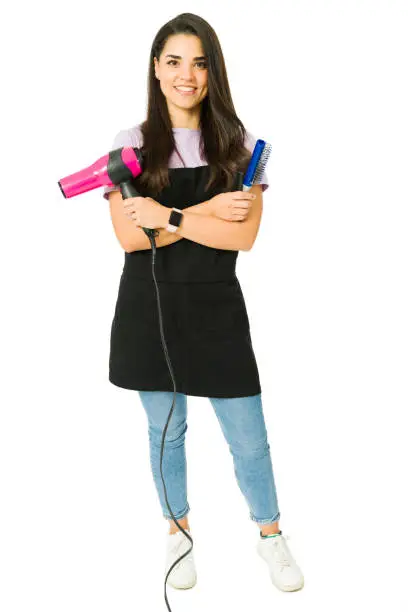 Cheerful young woman working as a hairdresser. Full length of a hairstylist using a hairbrush and blow dryer