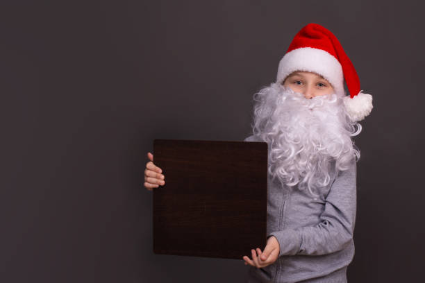 little santa is holding an empty board for copy space - christmas child little boys peeking imagens e fotografias de stock