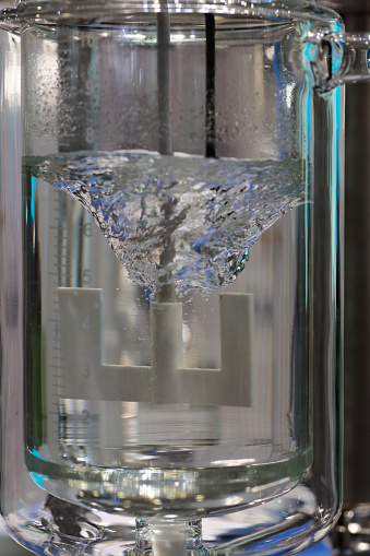 Mixing of liquid by an agitator with anchor blades. Laboratory glass reactor with stirrer. Selective focus.