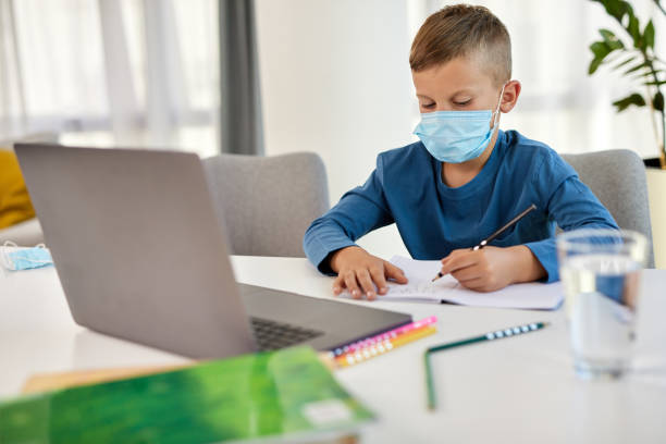 istock School boy with face mask watching online education classes on laptop 1353715010