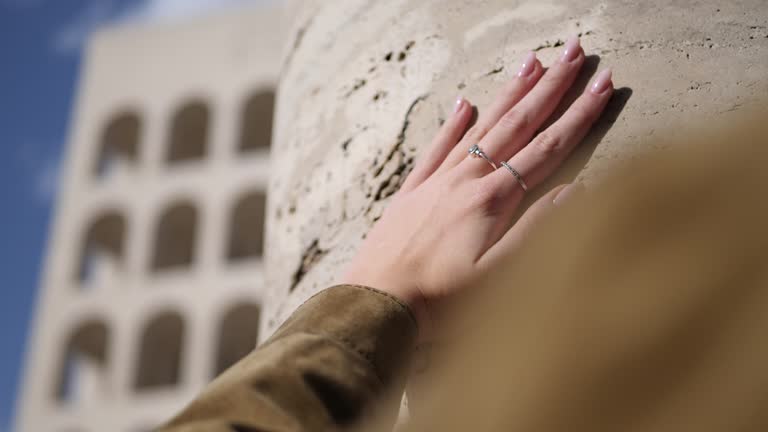 Hand stroking antique travertine marble column. Art and monuments. in the background the square colosseum in Rome.