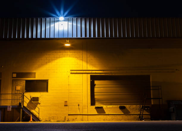 Yellow light shining on industrial warehouse wall at night stock photo