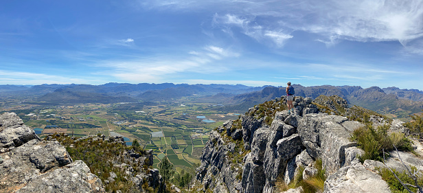 Panoramic of a woman standing on a rock admiring the view over the beautiful valley. Active woman enjoying a hike in nature living an active lifestyle.