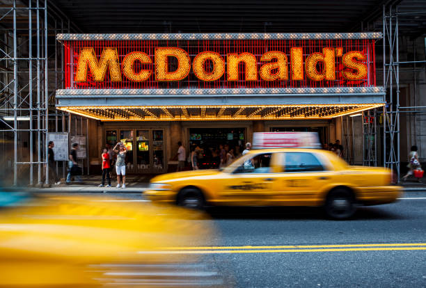 Large group of people and yellow taxis passing by at the entrance to McDonalds fast-food restaurant in Midtown Manhattan stock photo