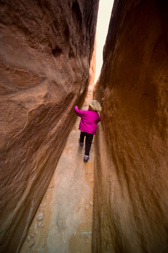 Little Girl Playing in Narrow Slot Canyon.  Toddler girl having fun in textured, red-rock narrow slot canyon in the desert southwest near Moab Utah USA.  Captured as a 14-bit Raw file. Edited in ProPhoto RGB color space.