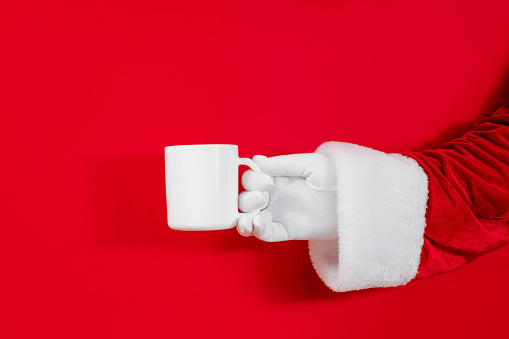 Christmas mockup of a white mug in Santa's hand on red background. Christmas concept, brand