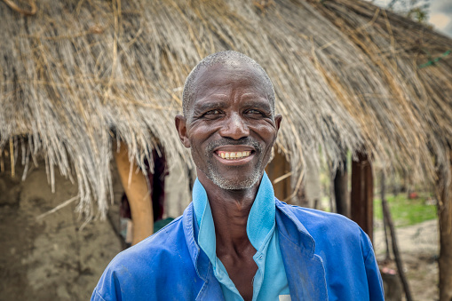 Happy elderly African man portrait, in front of his house in an African village
