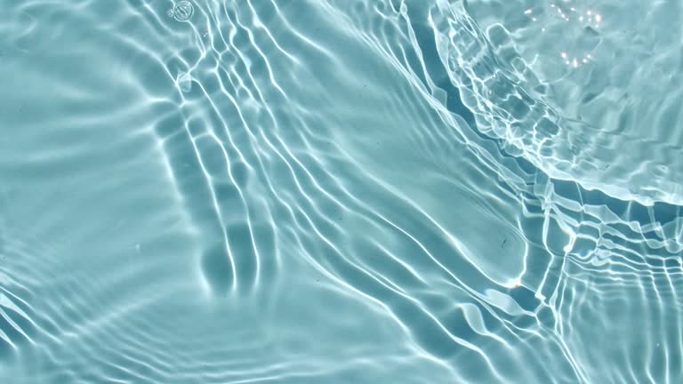 Water surface texture top view. Water splash blue colored. Pure blue water with reflections sunlight in slow motion. Sun and shadows. Motion clean swimming pool ripples and wave. 4k