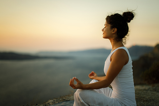 Relaxed woman doing Yoga meditation exercises in Lotus position on a hill above the sea. Copy space.