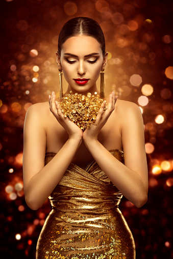 Fashion Beauty Model holding Golden Jewelry Flowers in Hands. Woman Face Hand Skin Care and Cosmetic over Shining Bokeh Lights Brown Background