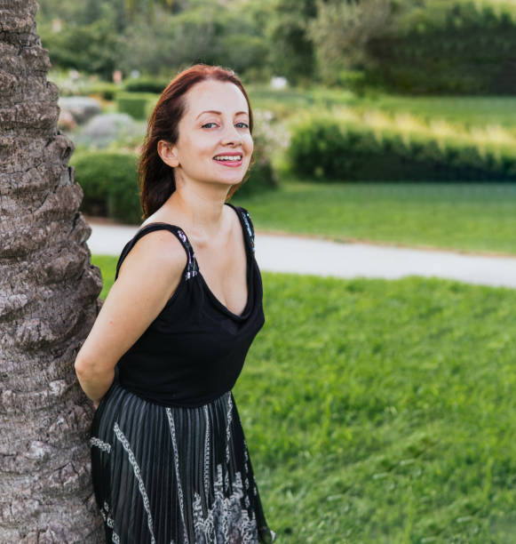 istock Dyed red haired blue eyed woman leaning on a palm tree smiling 1353756848
