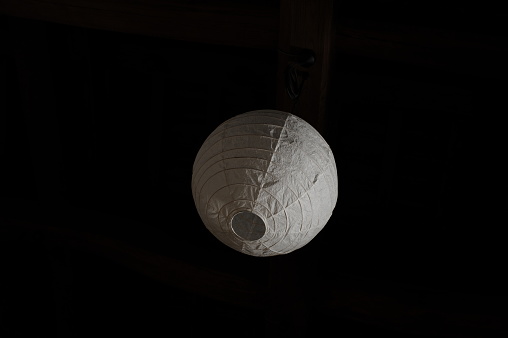 White paper handmade lamp or lampion hanging from the black ceiling in a studio