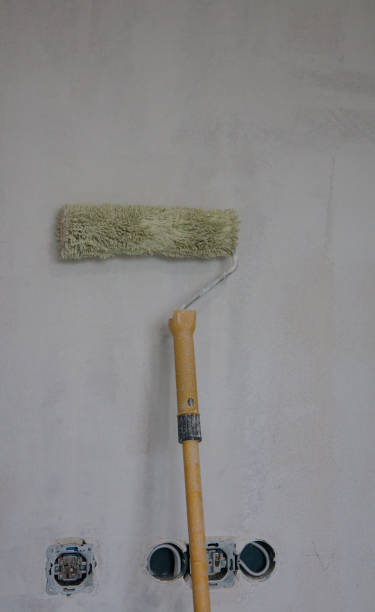 istock Painter's working tool, white paint roller leaning against the wall. 1353761296