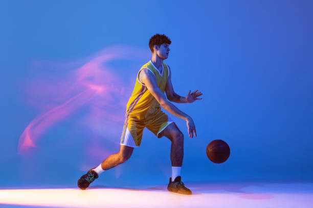 istock Dynamic portrait of professional basketball player training with ball isolated on blue studio background in mixed neon light. 1353761349