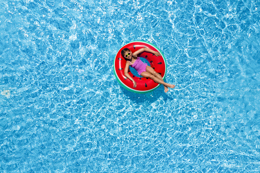 Cute little girl with inflatable ring in swimming pool, top view