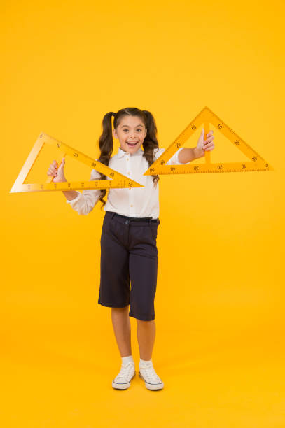 istock Learning geometry in school. School kid holding measuring instruments on yellow background. Cute little pupil preparing triangles for school lesson. Small girl is back to school 1353761983