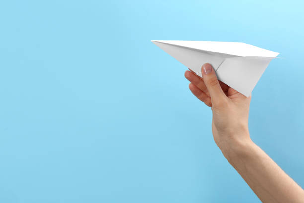 istock Woman holding paper plane on light blue background, closeup. Space for text 1353763454