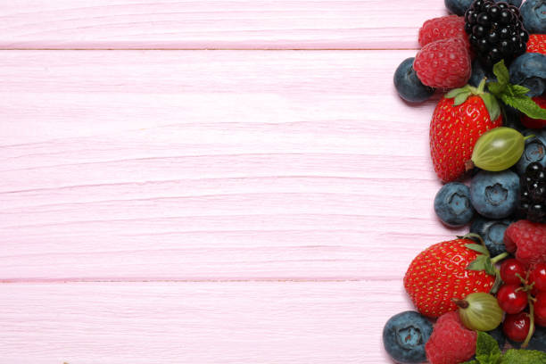 Mix of different fresh berries and mint on pink wooden table, flat lay. Space for text