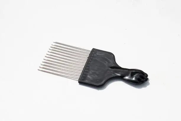 A black, plastic comb or Afro pick for textured hair with a fist on the end and silver teeth. The object is isolated against a white background.
