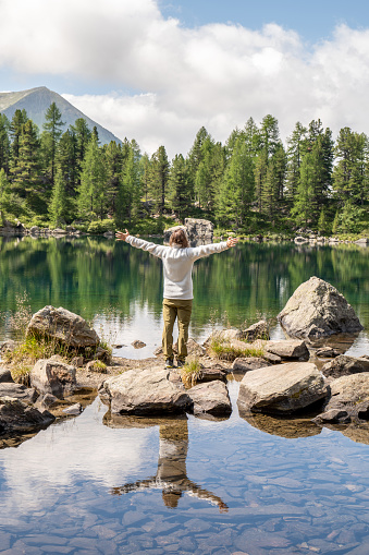 He relaxes in nature on a beautiful alpine lake in a middle of a pine tree forest in Graubunden canton, Switzerland