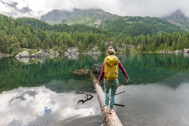 알프스 호수 위의 나무 줄기위를 걷고 있는 젊은 여성 - graubunden canton lake water travel destinations 뉴스 사진 이미지