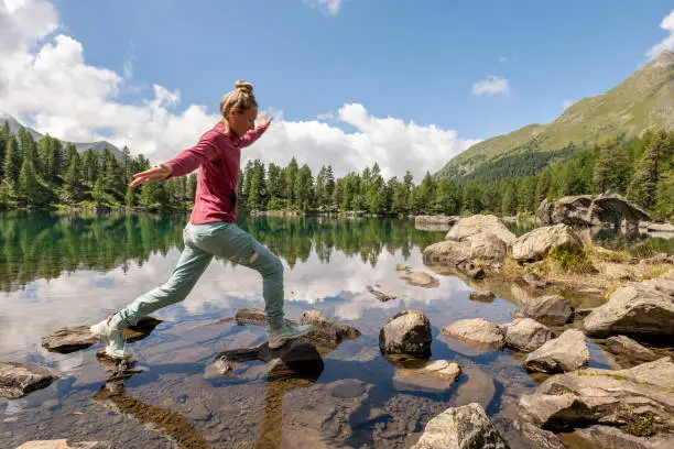Photo of Female hiker jumps from rock to rock above alpine lake