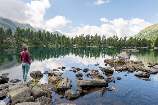 She relaxes in nature on a beautiful alpine lake in a middle of a pine tree forest in Graubunden canton, Switzerland