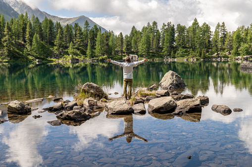 He relaxes in nature on a beautiful alpine lake in a middle of a pine tree forest in Graubunden canton, Switzerland