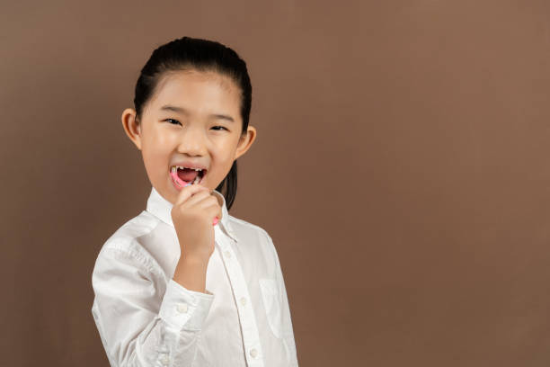 istock Little Girl Brushing Teeth on Brown Background 1353783743