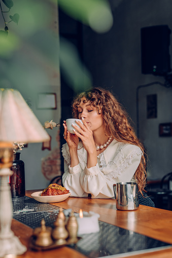 Young woman with curly hair wearing vintage style enjoy tea at the cafe. Selective focus on the woman.