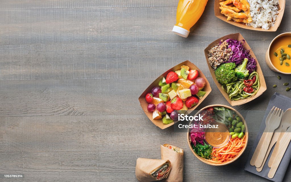 Healthy take away food and drink in disposable eco friendly paper containers Healthy take away food and drink in disposable eco friendly paper containers on gray wooden background, top view. Fresh salad, soup, poke bowl, vegetable, fruits, chicken wrap and juice. Healthy Eating Stock Photo