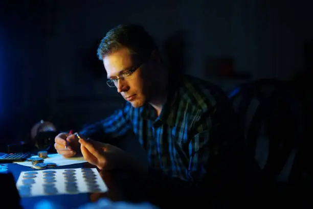 Photo of Male numismatist examines collection of coins.