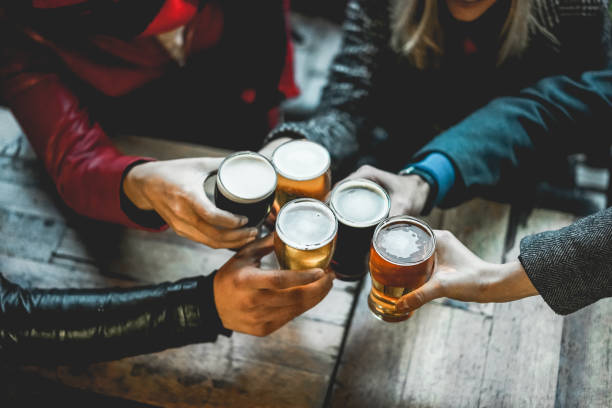 バーレストランで屋外でビールを楽しんで応援している人々の若いグループ - ガラスを握る右手にソフトフォーカス - beer ストックフォトと画像