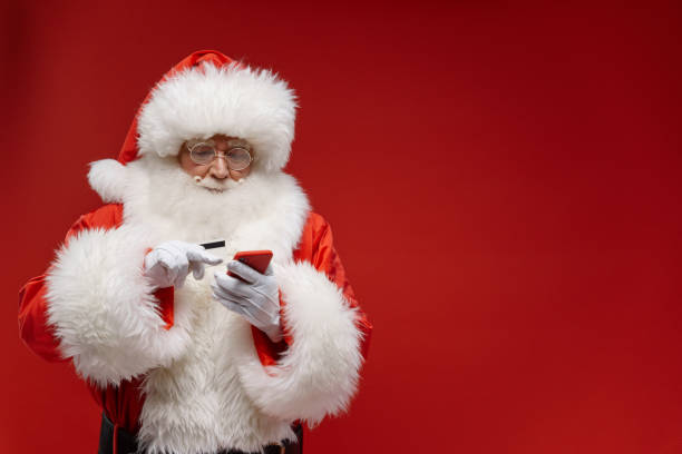 istock Santa Claus uses his red smart phone, standing on a red background 1353789307
