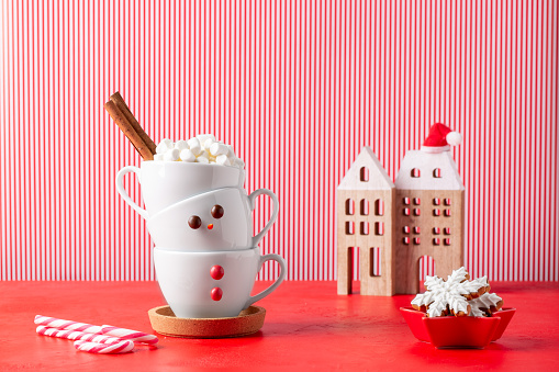 Tower of cups in form of snowman on red background. Hot chocolate with marshmallow and cinnamon. Traditional winter holiday drink. Merry Christmas and happy New year concept.