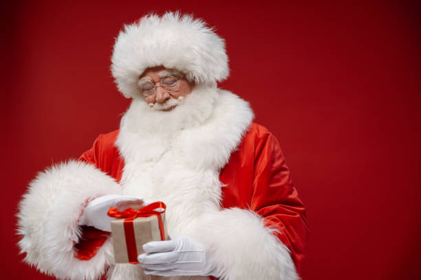 istock Kind Santa stroking a little gift box on a red background 1353789715