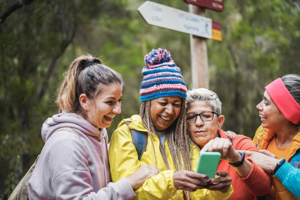 istock Multiracial women having fun using mobile phone while trekking in to the wood - Focus on african woman face 1353789893