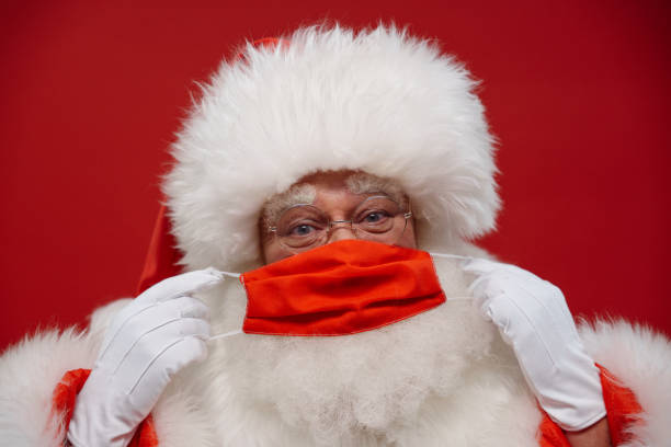 istock Santa Claus putting on a red protective face mask on a red background 1353790329