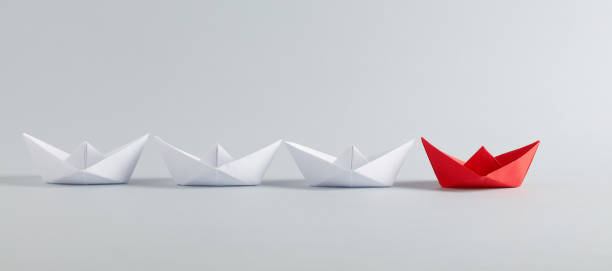 istock Red paper boat leads white paper ships. Leadership, collaboration, cooperation, or partnership in business 1353793385