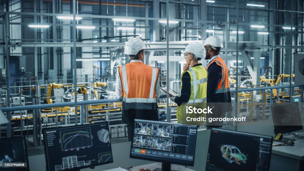 Young Diverse Team of Automotive Engineers Working in Office at Car Factory. Industrial Designer Talks About Electric Engine Parts with Colleagues, Discussing Different Technological Applications. Manufacturing Stock Photo