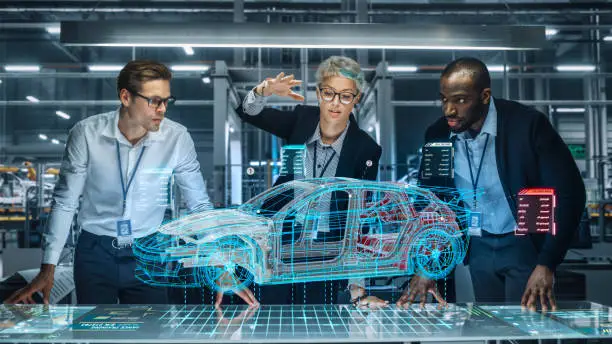 Photo of Diverse Team of Engineers Working in Office at Industrial Factory. Industrial Designers Discuss Electric Car Augmented Reality Hologramm. Specialists Work in Technological Car Development Facility.