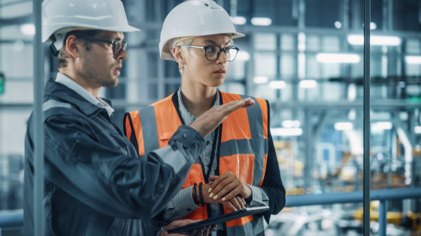 istock Male Engineer and Female Industrial Product Designer Discuss Work while Using Tablet in Office at a Car Assembly Plant. Industrial Specialists Working on Vehicle Design in Technological Factory. 1353796857