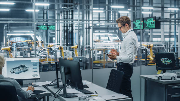 istock Handsome Engineer in Glasses and White Shirt Using Tablet Computer and Looking Out of the Office at a Car Assembly Plant. Industrial Specialist Working on Vehicle Design in Technological Facility. 1353796881