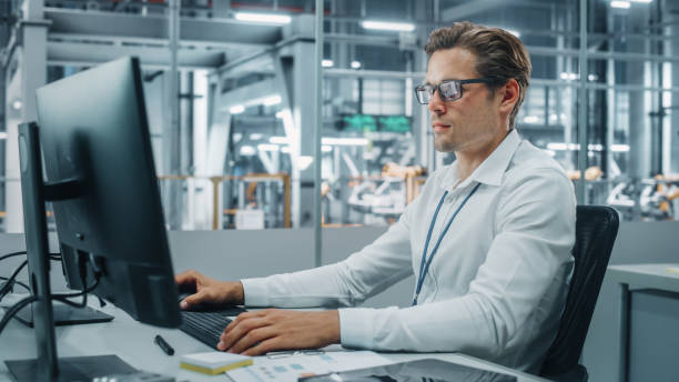 istock Confident Automotive Engineer Working on Desktop Computer in Modern Office at Car Assembly Plant. Industrial Project Manager Creating Sales, Finance and Marketing Reports at Vehicle Factory. 1353796890