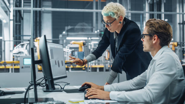 istock Two Automotive Engineers Discussing Concept Car Blueprints on Desktop Computer in Modern Office at Assembly Plant. Female Industrial Project Manager Talk to Male Designer at Vehicle Factory. 1353796899
