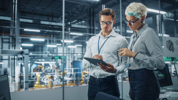 istock Male Engineer and Female Industrial Product Designer Discuss Work while Standing in Office at a Car Assembly Plant. Industrial Specialists Working on Vehicle Design in Technological Factory. 1353796933