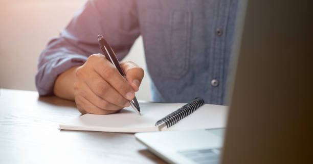 istock Close-up of man hand using writing pen memo on notebook paper or letter, diary on table desk office. 1353798173