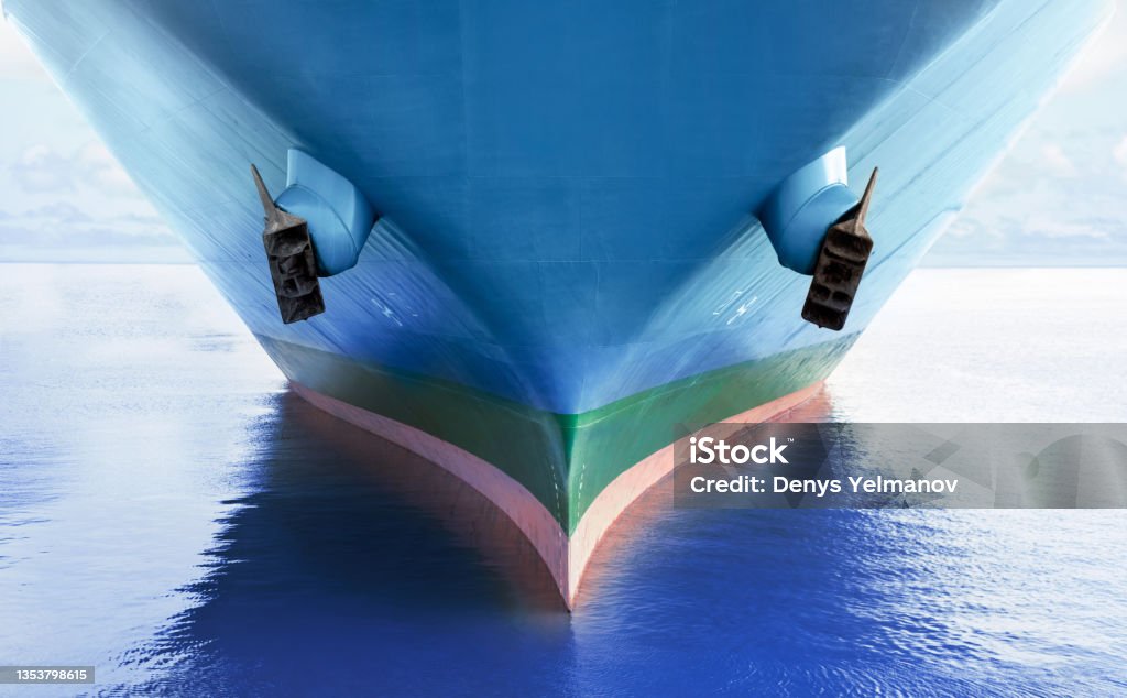 Front view of large blue merchant cargo ship in the middle of the ocean. Performing cargo export and import operations. Front view of large blue merchant cargo ship in the middle of the ocean. Performing cargo export and import operations with horizon line and beautiful sky. Ship Stock Photo
