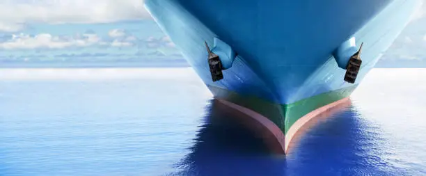 Photo of Front view of large blue merchant cargo ship in the middle of the ocean. Performing cargo export and import operations.