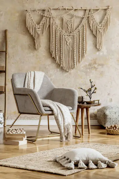Photo of Stylish oriental living room with design armchair, beautiful macrame, wooden ladder, decoration, carpet, coffee table, book and elegant personal accessories in wabi sabi concept.